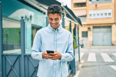 Genç Latin adam mutlu bir şekilde gülümsüyor ve şehirde akıllı telefon kullanıyor..