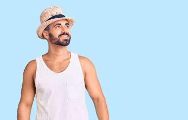 Gündelik yaz şapkası takan genç İspanyol adam yüzünde gülümsemeyle yan yana bakıyor, doğal bir ifade. Kendinden emin gülen. 