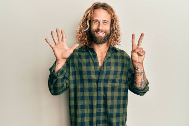 Sakallı, uzun saçlı, günlük kıyafetler giyen, yedi numaralı parmaklarıyla gösteriş yapan yakışıklı, kendinden emin ve mutlu bir adam.. 