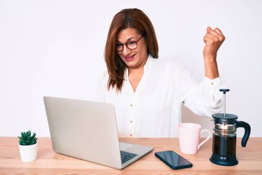 Orta yaşlı esmer, İspanyol iş kadını ofiste çalışıyor. Gururla bağırıyor, zaferi kutluyor ve başarıyı kollarını kaldırarak kutluyor. 