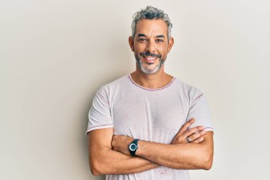 Orta yaşlı, gri saçlı, sıradan kıyafetler giyen mutlu yüzlü, kollarını kavuşturup kameraya bakan bir adam. pozitif kişi. 