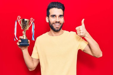 Sakallı, sakallı, mutlu ve pozitif gülümseyen genç bir adam. Başparmağıyla mükemmel ve onay işareti yapıyor. 