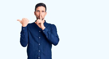 Gündelik tişört giyen genç yakışıklı adam sessiz olmak istiyor. Parmakları dudaklarında, elleri yandan işaret ediyor. sessizlik ve gizli konsept. 