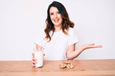 Genç, güzel esmer kadın bir bardak taze süt ve kurabiyelerle başarıyı kutluyor mutlu bir gülümsemeyle ve kazanan yüz ifadesini kaldırarak. 
