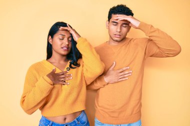 Güzel Latin genç çift günlük kıyafetlerini giyip hastalık, ateş, grip ve virüs için alnına dokunuyorlar. 