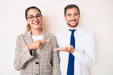 İş kıyafetleri giymiş güzel bir çift kameraya hayret içinde ve gülümserken elleri ve parmaklarıyla gösteriyorlar.. 