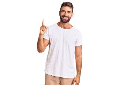 Gündelik beyaz tişört giyen genç İspanyol bir numaralı parmağını gösterip gösterirken kendinden emin ve mutlu bir şekilde gülümsüyor.. 