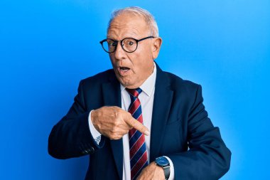 Kıdemli beyaz adam iş elbisesi ve kravat takıyor. Aceleyle saati gösteriyor. Sabırsız, sinirli ve son teslim tarihi geciktiği için kızgın. 