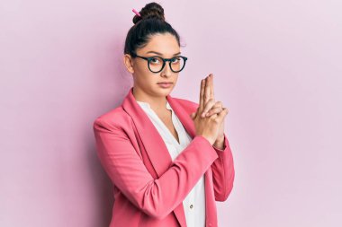 Güzel bir ortadoğulu kadın iş ceketi ve gözlük takıyor. Elinde sembolik bir silah var. El hareketleriyle cinayet silahlarıyla oynuyor. 