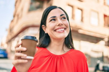 Genç Latin kız gülümsüyor. Mutlu bir şekilde içiyor. Kahve içiyor, şehirde yürüyor..