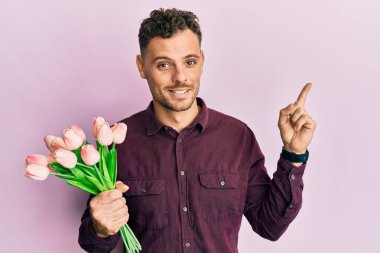 Genç İspanyol adam elinde pembe lalelerden bir buket çiçek tutarken mutlu bir şekilde gülümsüyor. 