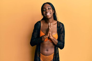 Genç Afro-Amerikalı kadın iç çamaşırı giyiyor. Elleriyle dua ediyor. Affedilmeyi diliyor.. 