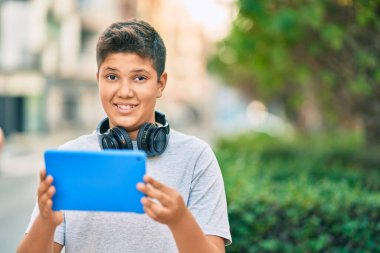 Sevimli Latin çocuk mutlu bir şekilde gülüyor. Parkta kulaklık ve dokunmatik ped kullanıyor..