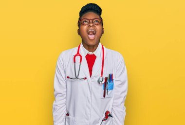 Genç Afro-Amerikalı kadın doktor üniforması giyiyor ve steteskop kızgın ve kızgın bağırıyor sinirli ve öfkeli, öfkeyle bağırıyor. öfke ve agresif konsept. 