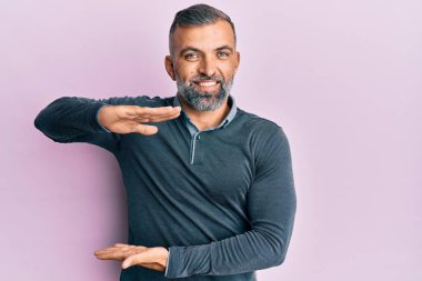 Orta yaşlı, sıradan kıyafetler giyen, elleri büyük ve büyük boy işareti gösteren, ölçü sembolü olan yakışıklı bir adam. Kameraya bakıp gülümsüyor. ölçüm kavramı. 