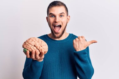 Beyni elinde tutan yakışıklı genç adam başparmağını yana kaldırıyor ve ağzı açık gülümsüyor. 