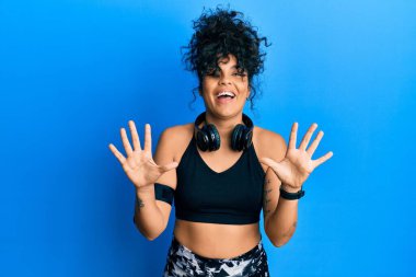 Spor kıyafetleri giyen ve kulaklık takan genç İspanyol kadın on numarayı gösterip işaret ederken kendinden emin ve mutlu bir şekilde gülümsüyor.. 