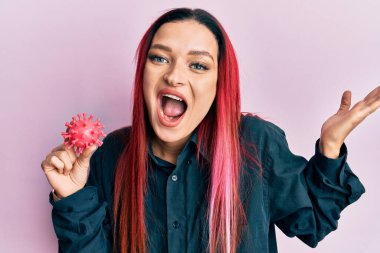 Virüs oyuncağı taşıyan genç beyaz kadın zaferi mutlu bir gülümsemeyle ve kazanan yüz ifadesiyle kutluyor. 