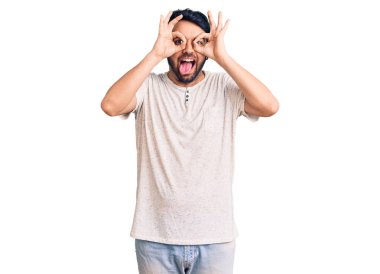 Günlük kıyafetler giyen genç İspanyol adam dürbün gibi jest yapıyor. Dürbün dilini çıkarıyor, gözler parmaklarından bakıyor. çılgın ifade. 