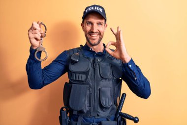 Üniforma giyen yakışıklı bir polis memuru ve sarı arka planda kelepçeli bir kurşuncu. Parmaklarıyla işaret veriyor, gülümsüyor.