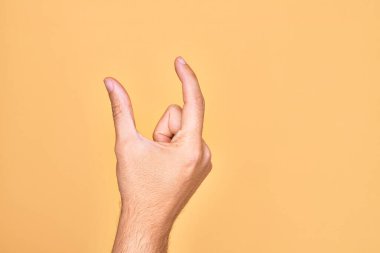 İzole edilmiş sarı arka plan üzerinde parmaklarını gösteren beyaz bir adamın eli. Görünmez bir şeyi alıp, parmaklarıyla uzayı gösteren bir nesneyi tutuyor.