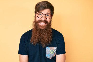 Uzun sakallı, sıradan kıyafetler ve gözlüklü yakışıklı genç adam pozitif ve mutlu görünüyor ve kendine güvenen bir gülümsemeyle dişlerini gösteriyor. 