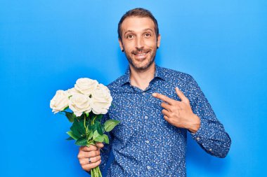 Çiçekleri tutan yakışıklı genç adam mutlu bir şekilde elini ve parmağını gösterdi. 