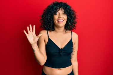 Kolsuz tişörtlü, gündelik giyinen genç İspanyol kadın beş numaralı parmaklarıyla gülümseyerek kendinden emin ve mutlu bir şekilde işaret ediyor.. 