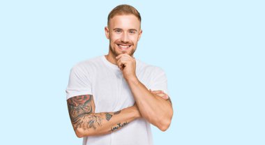 Sıradan kıyafetler giyen genç İrlandalı kameraya kendinden emin kollarını kavuşturup gülümseyerek ve çenesini kaldırarak bakıyor. Olumlu düşünmek. 