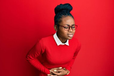 Genç Afro-Amerikalı kadın günlük kıyafetler giyiyor ve elleri karnında gözlükler takıyor çünkü mide bulantısı, acı verici bir hastalık kendini iyi hissetmiyor. Ağrı kavramı. 