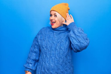 Genç, sarışın ve cüsseli bir kadın mavi balıkçı yaka kazak ve yün şapka giyip kulağı açık gülümsüyor ve dedikodu ya da dedikoduları dinliyor. Sağırlık kavramı.