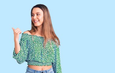 Gündelik tişört giyen, gülümseyen, gülümseyen, gülümseyen ve baş parmağıyla yan tarafı gösteren güzel bir kız.. 