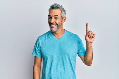 Orta yaşlı, gri saçlı, günlük kıyafetler giyen bir numaralı parmağı gösteren ve gülümseyen, kendinden emin ve mutlu bir adam.. 