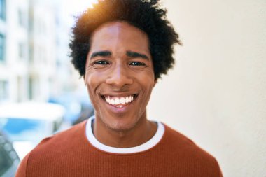 Genç, yakışıklı, Afro-Amerikan bir adam günlük giysiler giyip mutlu gülümsüyor. Yüzünde gülümsemeyle kasaba caddesinde yürürken.