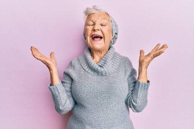 Yaşlı, gri saçlı, yün kazak giyen ve kış şapkalı bir kadın. Başarı için çılgın ve çılgın kutlamalar yapıyor. Kolları havada ve gözleri kapalı, heyecanlı çığlıklar atıyorlar. Kazanan konsept 