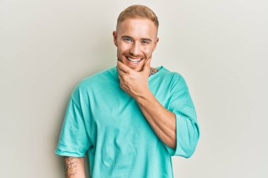 Gündelik kıyafetler giyen genç beyaz adam kameraya kendinden emin bakıyor kollarını kavuşturmuş ve çenesini kaldırmış gülümsüyor. Olumlu düşünmek. 