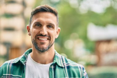 Genç beyaz adam gülümseyerek şehirde mutlu mesut duruyor..