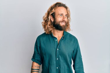 Sakallı, uzun saçlı, sıradan kıyafetler giyen, rahat bir görünüm takınan, kendine güvenen ve gülümseyen yakışıklı bir adam.. 