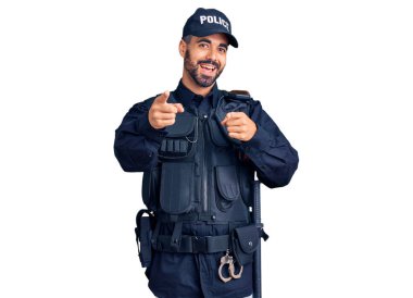 Polis üniforması giyen genç İspanyol adam mutlu ve komik yüzüyle kamerayı işaret ediyor. iyi enerji ve titreşimler. 
