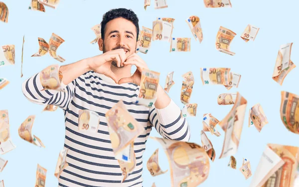 Gündelik kıyafetler giyen, aşık gülümseyen, elleriyle kalp sembolü yapan genç bir İspanyol. romantik kavram.