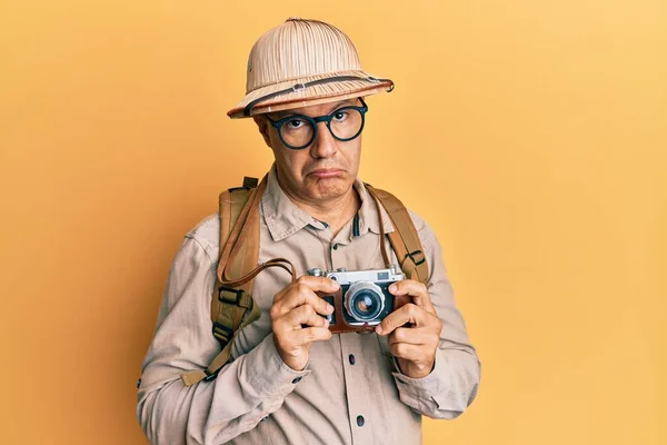 Middle age bald man wearing explorer hat and vintage camera depressed and worry for distress, crying angry and afraid. sad expression.