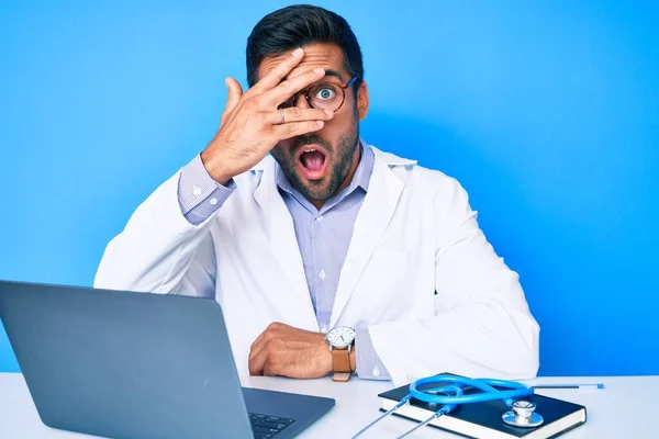 Young Hispanic Man Wearing Doctor Uniform Working Clinic Peeking Shock — Stock Photo, Image