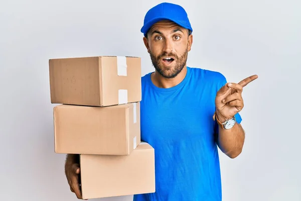 Handsome Man Beard Wearing Courier Uniform Holding Delivery Packages Surprised — Stock Photo, Image