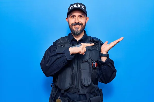 Young handsome man wearing police uniform amazed and smiling to the camera while presenting with hand and pointing with finger.