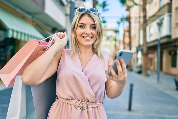 Genç Sarışın Kadın Gülümsüyor Alışveriş Torbaları Tutuyor Şehirde Akıllı Telefon — Stok fotoğraf