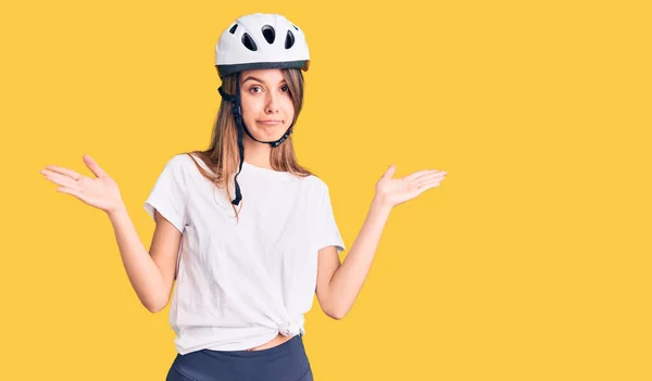 年轻美丽的女孩戴着自行车头盔 毫无头绪 满脸困惑 胳膊和双手高举 怀疑概念 — 图库照片