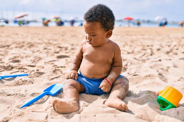 愛らしいアフリカ系アメリカ人の幼児はおもちゃで遊んでいます砂の上に座ってビーチ — ストック写真