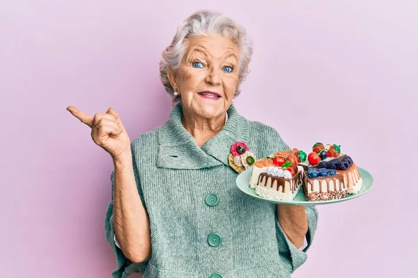 高个子灰白头发的女人拿着蛋糕盘 高兴地微笑着 手指手画脚地指向旁边 — 图库照片