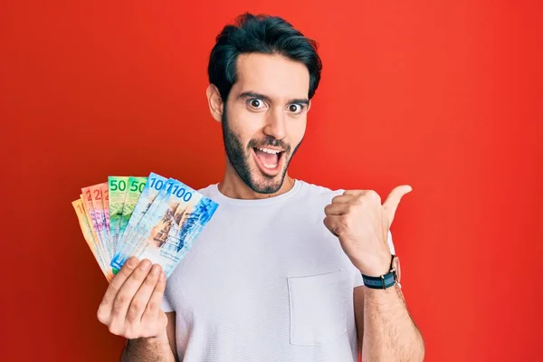 Joven Hispano Sosteniendo Billetes Franco Suizos Apuntando Con Pulgar Hacia —  Fotos de Stock