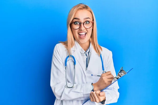 Mulher Loira Branca Bonita Vestindo Estetoscópio Médico Segurando Prancheta Celebrando — Fotografia de Stock